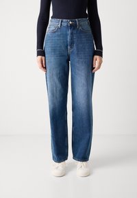 Jeans i medium blå med rett ben og høy midje. Har knapplukking, sidelommer og subtil falming på lårene.