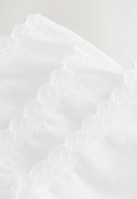 Tessuto bianco con un bordo in pizzo scallopato testurizzato, caratterizzato da cuciture fini e superficie liscia, che mette in risalto dettagli di design delicati.