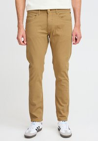 Khaki puuvillahousut suoran lahkeen designilla, viisi taskua ja nappikiinnitys. Yhdistetty valkoisten lenkkareiden kanssa, joissa on mustia raitoja.