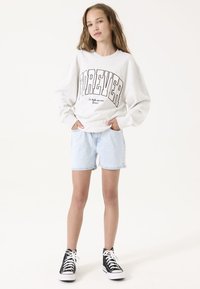 Sudadera gris clara con la palabra "FOREVER" en letras negras en negrita, combinada con pantalones cortos de mezclilla azul claro y zapatillas de deporte negras de caña alta. Diseño simple.