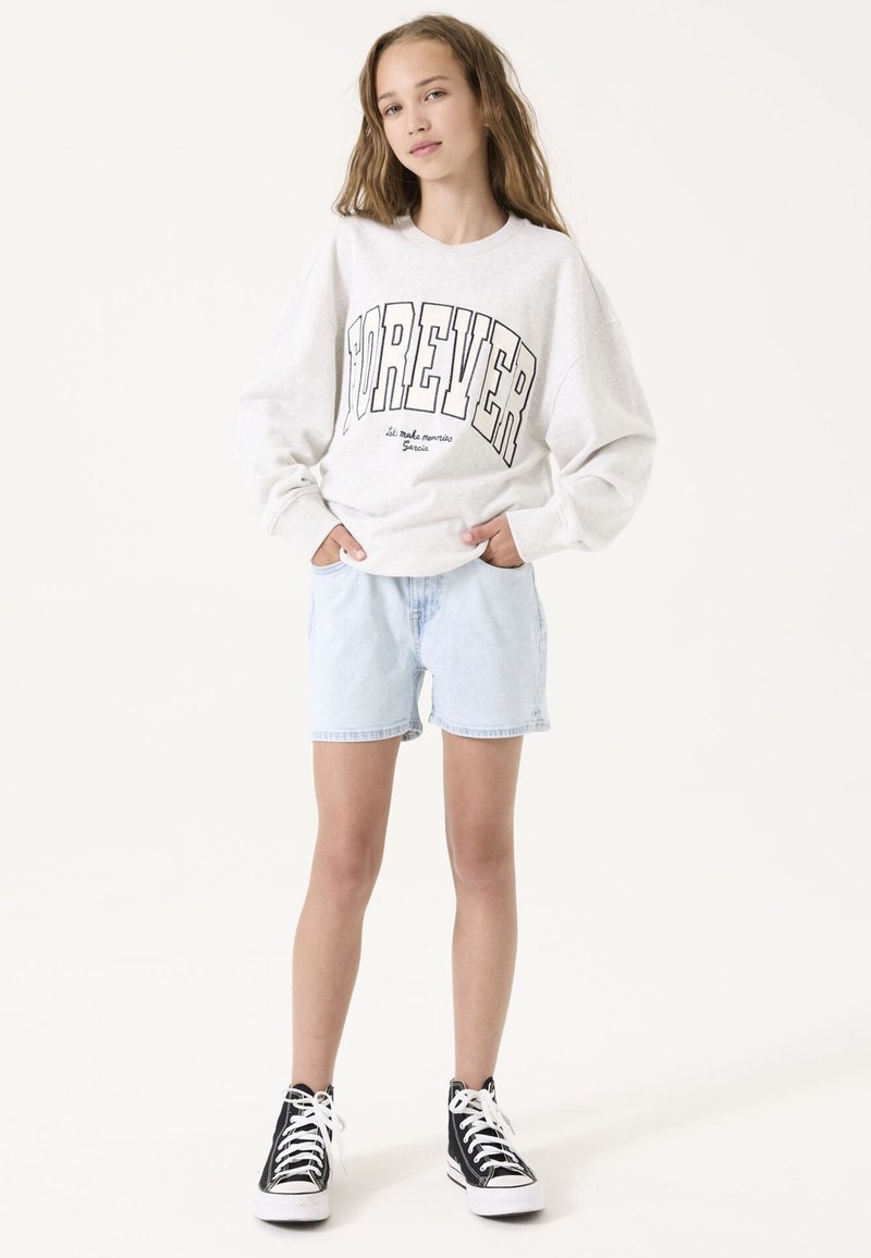 Sudadera gris clara con la palabra "FOREVER" en letras negras en negrita, combinada con pantalones cortos de mezclilla azul claro y zapatillas de deporte negras de caña alta. Diseño simple.