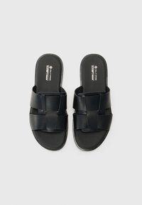Crne veganske natikače s križastim trakama, glatkom teksturom i ravnim potplatom. Minimalistički stil s elegantnim izgledom.