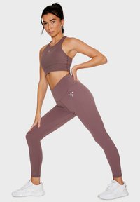 Gelaagde sportbeha en high-waisted leggings in mauve stof, met een gladde textuur en een aansluitend ontwerp, met een logo-accent op de legging.