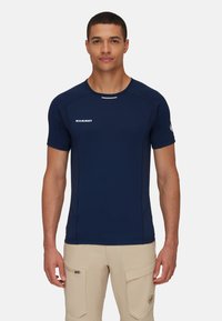 Marineblauw sportshirt met korte mouwen en een ronde hals, vlakke naden en een wit logo op de voorkant. Lichtgewicht, vochtafvoerende stof.