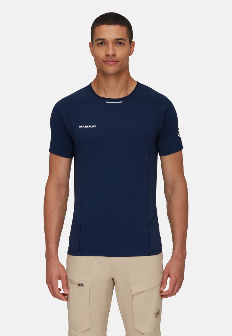 Marineblauw sportshirt met korte mouwen en een ronde hals, vlakke naden en een wit logo op de voorkant. Lichtgewicht, vochtafvoerende stof.