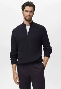 Marine blauw zip-up trui met ribbeltextuur, staande kraag en zilveren rits. Gecombineerd met zwarte broeken met aansluitende mouwen.