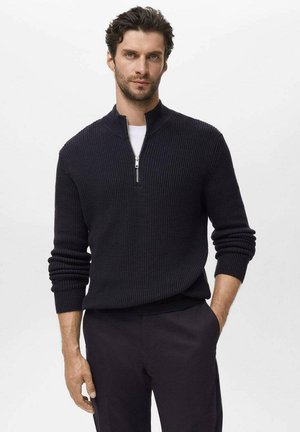 Marine blauw zip-up trui met ribbeltextuur, staande kraag en zilveren rits. Gecombineerd met zwarte broeken met aansluitende mouwen.