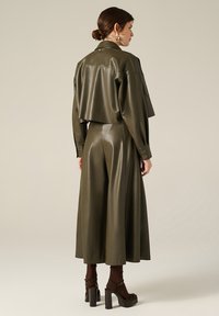Giacca in ecopelle verde oliva con design corto, pantaloni larghi e sandali con tacco spesso. Finitura satinata e dettagli con bottoni.