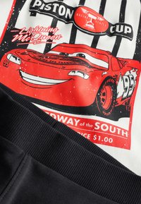 Valge kangas, millel on trükitud punane võidusõiduauto graafika. Alumises osas mustad aktsendid ja sooniline tekstuur. Tekst sisaldab sõnu "Piston Cup" ja "Lightning McQueen".