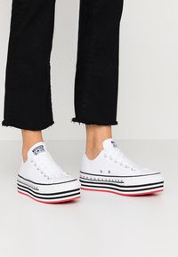 Vita canvas plattformssneakers med svart och röd randig gummisula, silverfärgade ögla och signaturlogotyp på tungan.