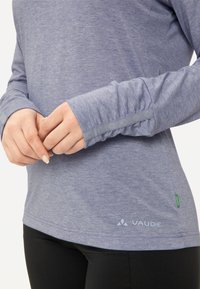 Langärmliges lila Sportoberteil aus strukturiertem Stoff, mit einem Logo und grünen Akzenten. Die Bündchen haben dezente Details und eine lockere Passform.