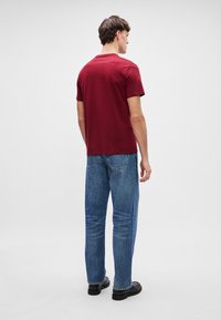 Maroon ümar kaelusega T-särk, lühikeste varrukatega, koos helesiniste sirgete pükstega, mustad kingad, esitatud tagantpoolt lihtsal taustal.