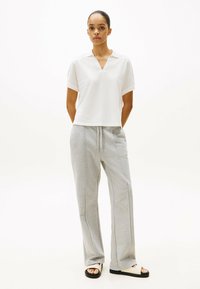 Witte polo met korte mouwen en v-hals, gecombineerd met lichtgrijze joggingbroeken met zijnaad en zwart-witte slides.