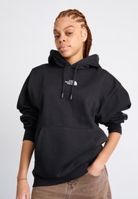 Sweat-shirt à capuche noir avec une poche avant et le logo blanc de The North Face. Le tissu semble doux avec une coupe décontractée et des poignets côtelés.