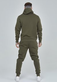Olivgrünes Hoodie- und Jogginganzug-Set aus weichem, strukturiertem Stoff. Verfügt über eine Kapuze, lange Ärmel sowie elastische Bündchen und Bund.