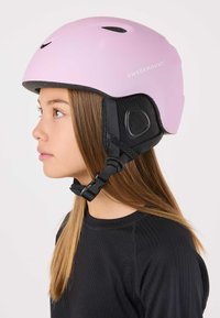 Pink helmet with matte finish, adjustable chin strap, and black mesh ear pads. Features branding on the side and ventilation holes.