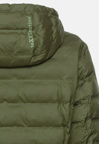 Oliven grøn pufferjakke med høj krave, quiltet tekstur og et logo trykt på skulderen. Stoffet ser glat og skinnende ud.
