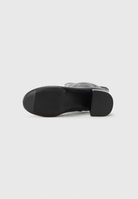 Bottine en cuir noir avec un bout carré, une semelle texturée et un talon bloc. Caractérisée par une surface lisse et un design minimaliste.