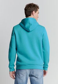 Turquoise hoodie met een zachte textuur, geribde manchetten en zoom, en een relaxte pasvorm. Zichtbare naden en een capuchondetail aan de achterkant.