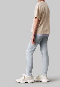 Beige bavlněné tričko s volným střihem, spárované s světle modrými skinny džíny. Obuv je bílá s logem, což ukazuje na ležérní, vrstvený vzhled.