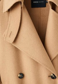 Tan double-breasted coat made of soft wool blend with large black buttons and notched collar, featuring a textured finish.