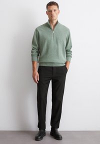Hellgrüner Reißverschluss-Pullover mit gerippten Bündchen und Saum, kombiniert mit schwarzen Nadelstreifen-Hosen und schwarzen Ankle Boots. Einfaches modernes Design.