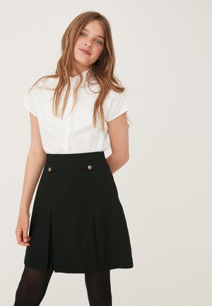 Hvid kortærmet skjorte med knaplukning, parret med en sort plisseret nederdel med to guldknapdetaljer.