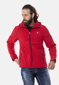 Rote Softshell-Jacke mit tailliertem Design, Reißverschluss vorne, zwei schwarzen Reißverschluss-Seitentaschen und Kapuze mit verstellbaren Kordeln.