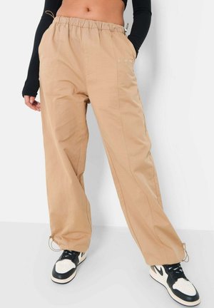 Beige afslappede bukser med elastisk talje, sidelommer og snore ved anklerne. Glat stof med subtile syninger.