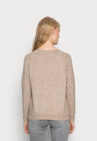 Beige strikkegenser med rund hals, lange ermer og ribbestrikket kant. Myk tekstur, avslappet passform, vist fra baksiden. Brukt med grå jeans.