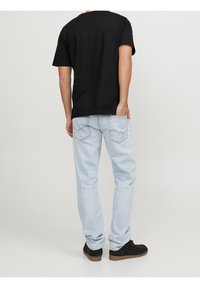 Camiseta de algodón negra y jeans de denim claro. Los jeans tienen bolsillos traseros con costuras curvas. Se llevan con zapatos de ante negros.