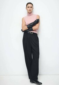 Uska ružičasta prsluk s rolkom bez rukava, crne hlače visokog struka s naborima, crne kožne rukavice i šiljate crne cipele; minimalistički dizajn.