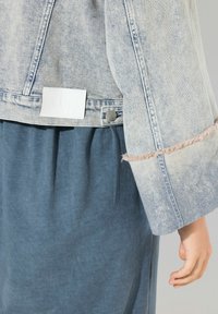 Ljusblå denimjacka med fransade ärmslut och en vit etikett. Matchad med en lös, mörkblå kjol i tyg.