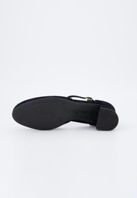 Zapato de mujer de ante azul marino con una correa al tobillo, que presenta una suela de goma negra y un tacón bajo. Marcado con la marca "Paul Green".