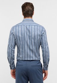 Blauw-witte gestreepte blouse met lange mouwen en knoopdetails. Heeft een klassieke kraag en een gestructureerde stof en wordt gedragen met blauwe pantalon.