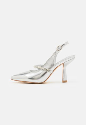 Chaussure à talon mi-haut argenté métallisé, à bout pointu, avec une bride décorative en strass. Texture lisse avec une finition brillante.