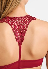 Bordeaux bh met ingewikkeld kantdetail op de rug, met bloempatronen en een soepele band. Verstelbare bandjes maken het ontwerp af.