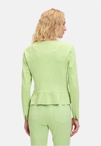 Jasnozielona marynarka skrojona z długimi rękawami, zaprojektowana w stylu peplum, z teksturowanej tkaniny, zestawiona z dopasowanymi spodniami.