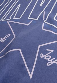 Μπλε ύφασμα με υφή που διαθέτει λευκό και ανοιχτό μπλε γραφικό κείμενο και σχεδιασμό αστεριού, προσθέτοντας οπτικό ενδιαφέρον και λεπτομέρεια.