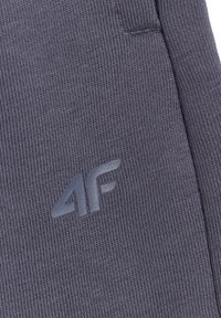 Tissu gris foncé avec un motif tricoté texturé présentant un logo 4F en relief près d'une couture ou d'un bord.