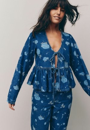 Denim peplum top with a deep V-neck, floral print in light blue, tie-front detail, long sleeves with elastic cuffs. Paired with matching jeans.