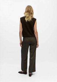 Braunes ärmelloses Stricktop, kombiniert mit hochgeschnittenen, taillierten olivgrünen Hosen und dunkelbraunen Ballerinas, von hinten betrachtet.