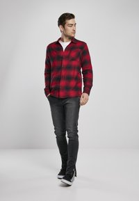 Rød og svart rutete flanellskjorte med knapper, brukt over en hvit T-skjorte, kombinert med mørke skinny jeans og svart-hvite sneakers.