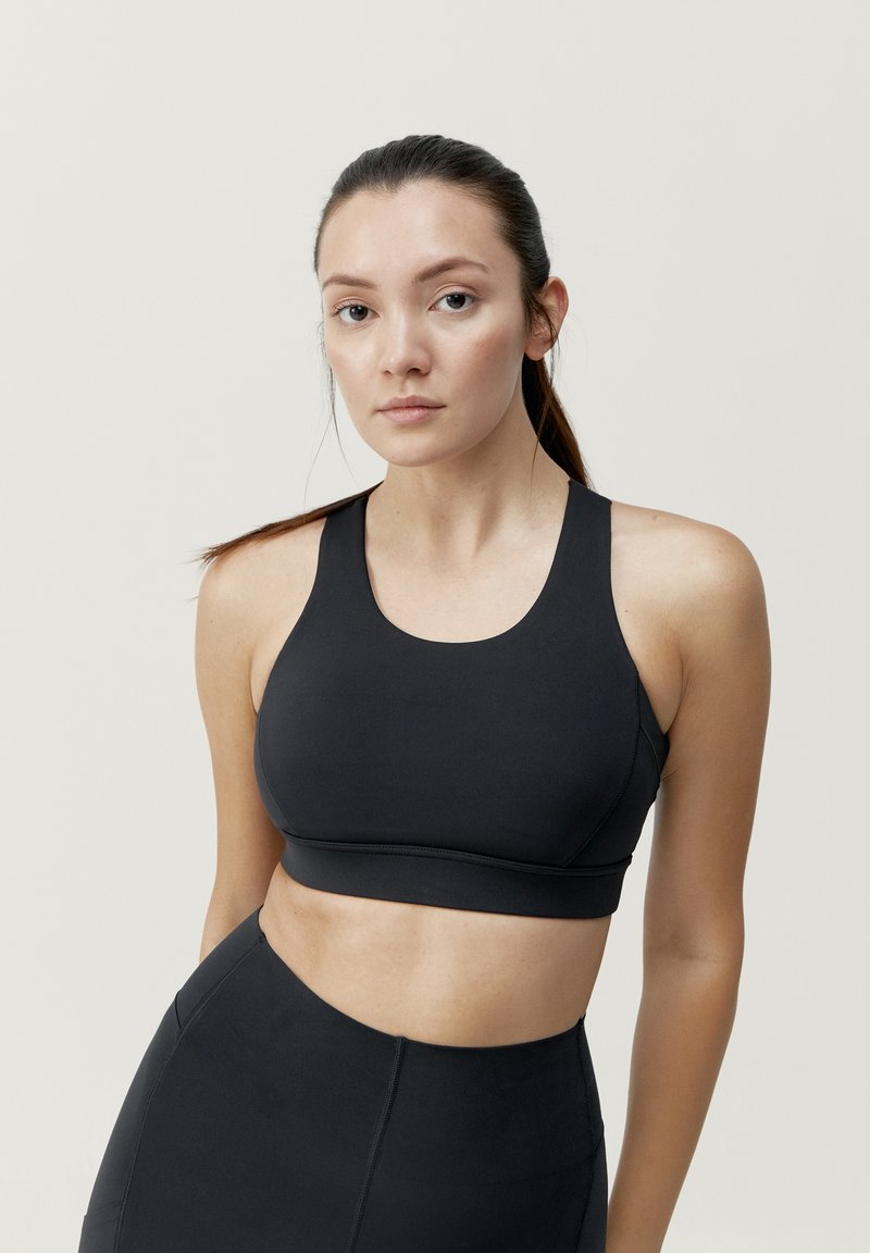 Čierna športová podprsenka z hladkej tkaniny, s guľatým výstrihom a širokými ramienkami. Obsahuje priliehavý strih pre podporu.