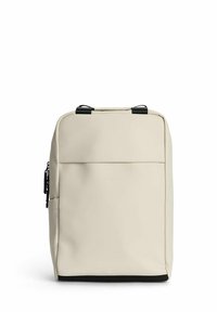 Beige ryggsäck tillverkad av slätt material, med rektangulär form, topphandtag och en framfick med dragkedja och minimalistisk logga.