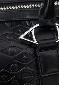 Black leather handbag with embossed circular and eye patterns; features a silver metallic triangle hardware detail and a zip closure.