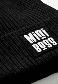 Black knitted beanie with a ribbed texture, featuring a rectangular black fabric patch with "Mini Boss" in bold white lettering.