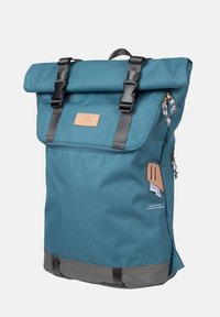 Teal plecak z podwijanym wierzchem, wykonany z trwałego materiału, z czarnymi klamrami, skórzaną łatą i szarymi akcentami na dole. Zawiera boczną kieszeń na zamek.