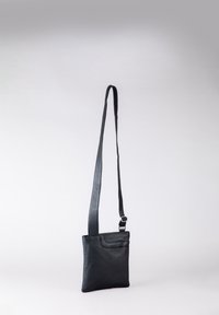 Black leather crossbody bag with a smooth texture, adjustable strap, and a front pocket. Minimalist design with a subtle logo detail.
