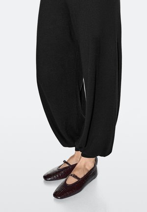 Zwarte, loszittende broek met een zachte textuur, gecombineerd met bordeauxrood kroko-geëmbossede flats met een bandje en een puntige neus.